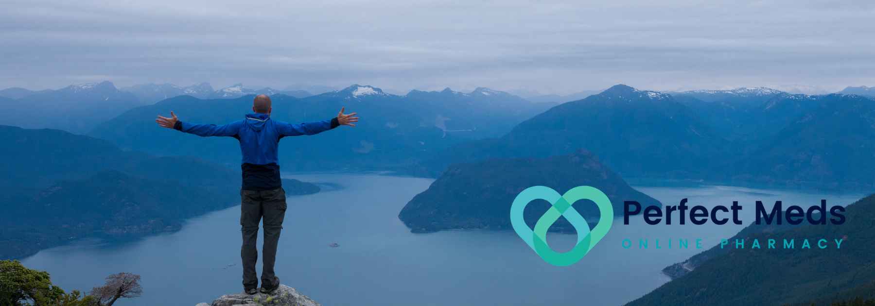male tourist in blue jacket admiring view of lake and mountains with arms outstretched